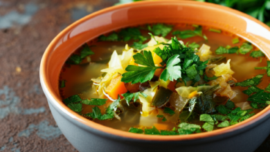 A bowl of vibrant vegetable soup, garnished with fresh parsley and herbs, set on a rustic table. The soup looks hearty and inviting, with visible pieces of cabbage and carrots.